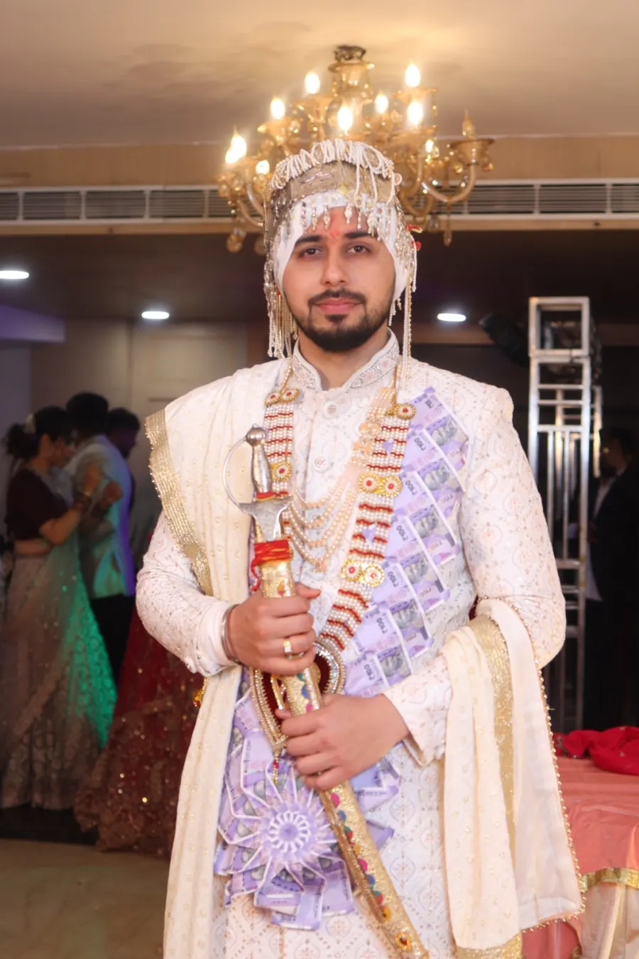 Groom under a gold chandelier, ceremonial sword in hand
