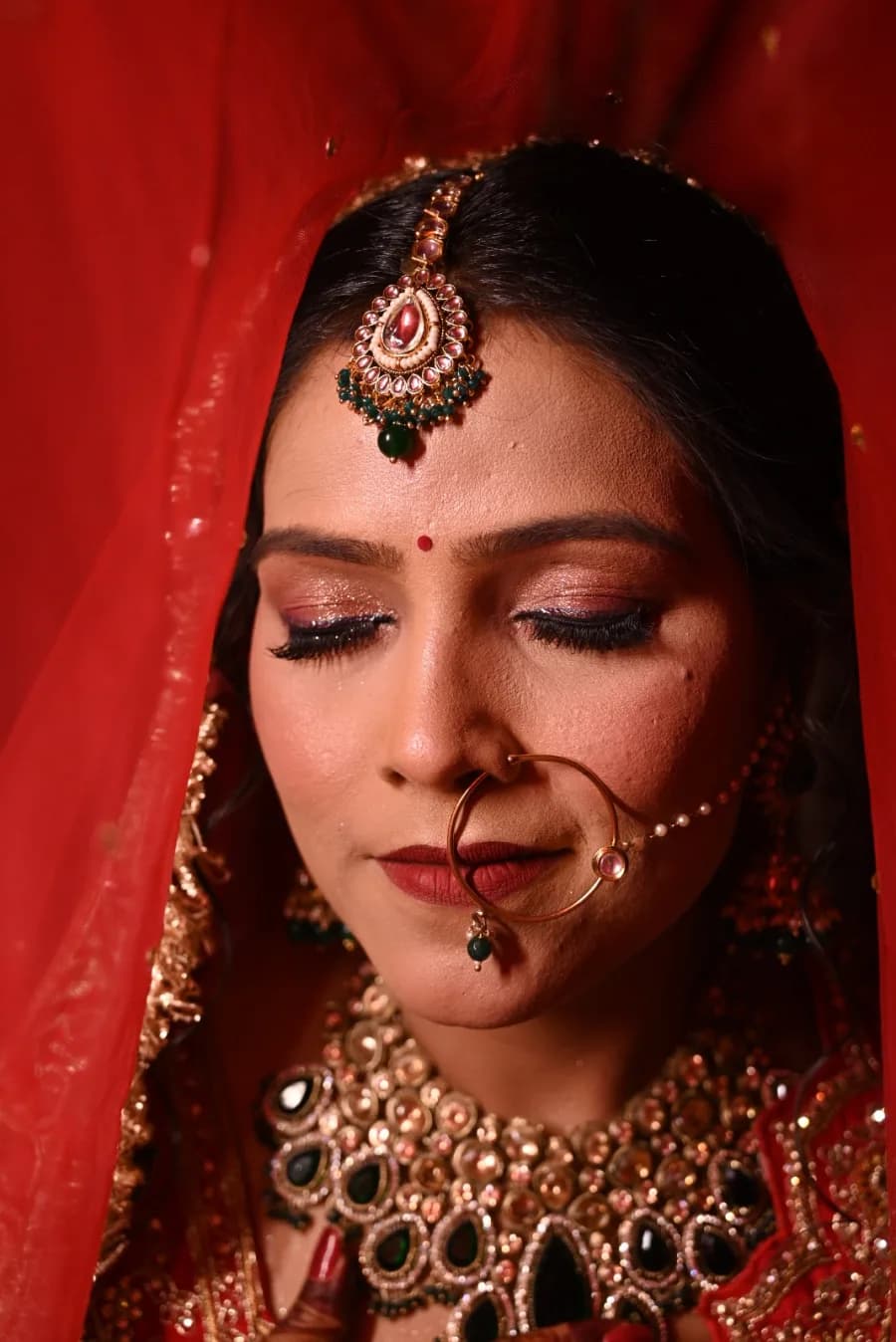 Close-up bridal portrait, eyes closed, framed by a red dupatta