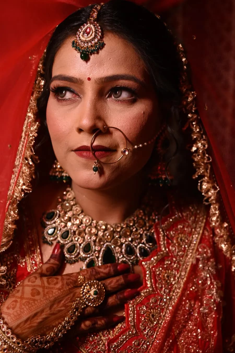 Bride glancing sideways in statement jewelry and a red veil