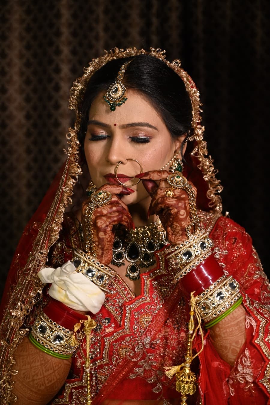 Bride with hands folded near her face, mehendi and bangles on display