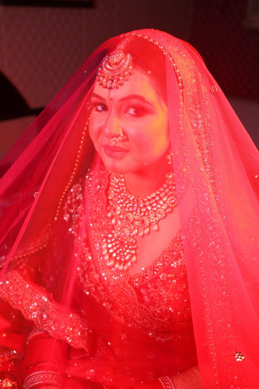 Bride under a sheer red veil, jewelry catching the light