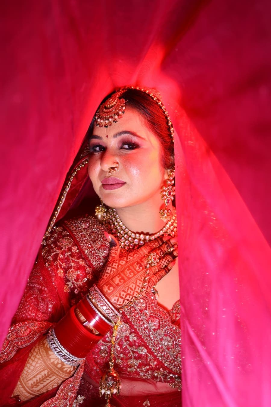 Bride peeking out from beneath the red dupatta