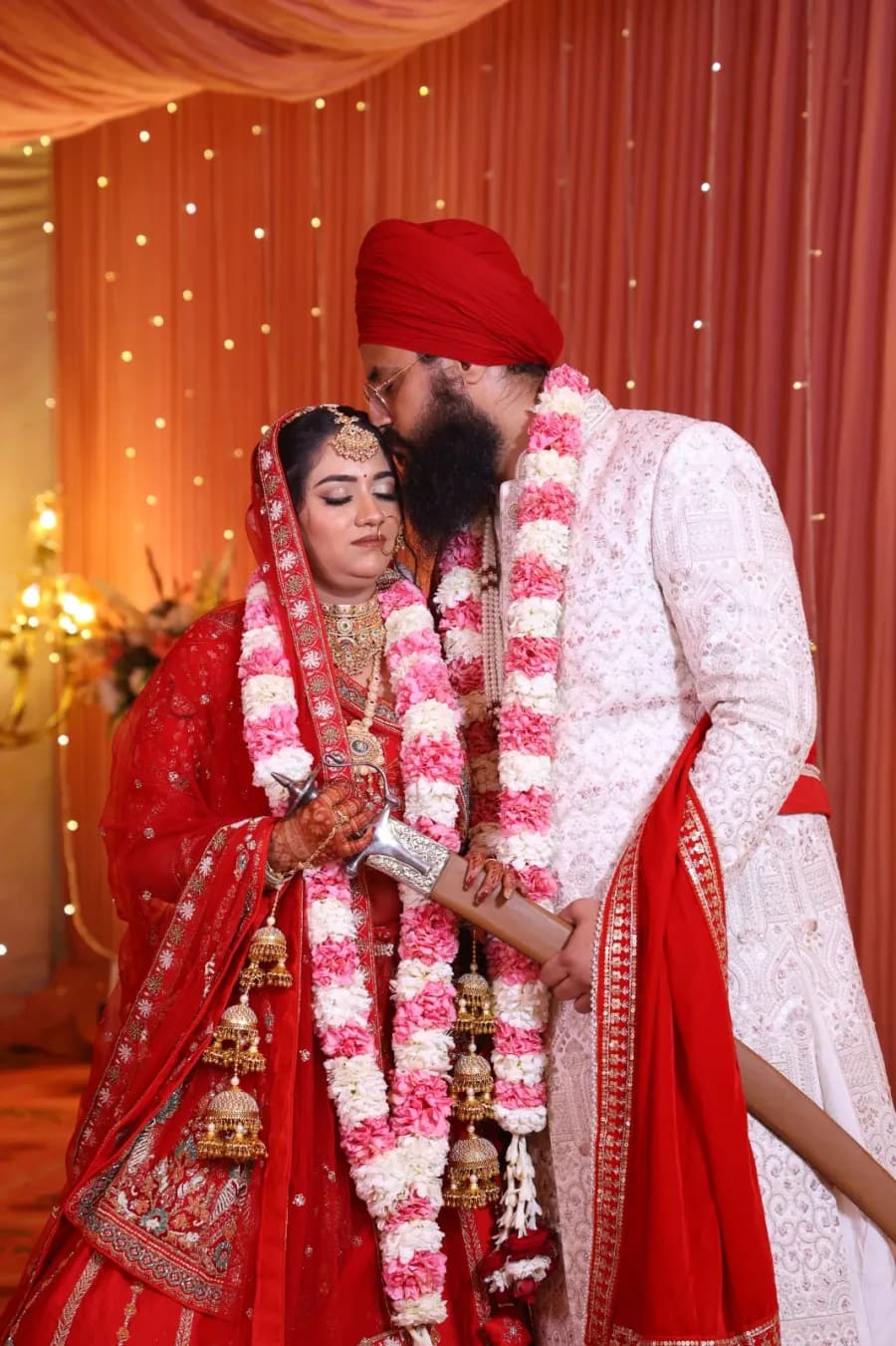 Groom placing a kiss on the bride’s forehead amid the garlands