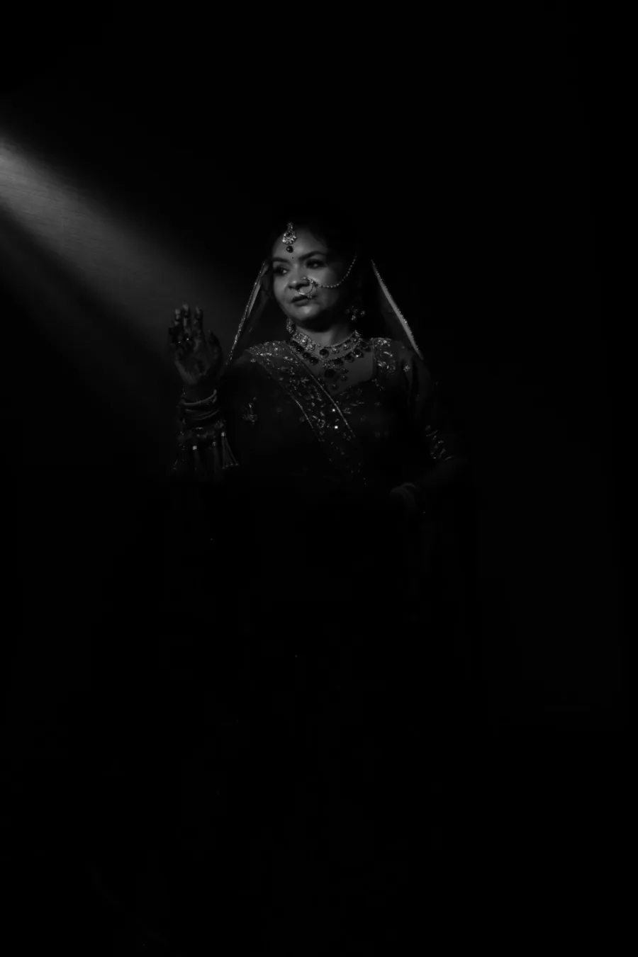 Bride silhouetted in a single beam of light, hand raised in a graceful pose