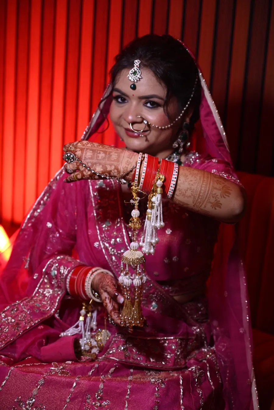 Bride adjusting her jewelry, red-lit studio backdrop