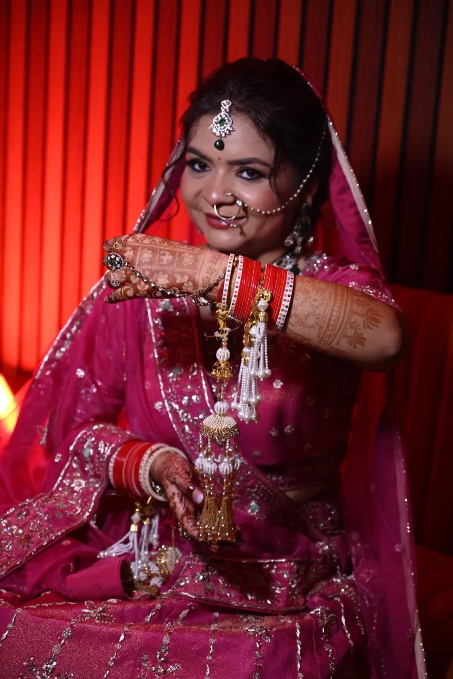 Bride mid-gesture with mehendi and bangles on display, warm studio light